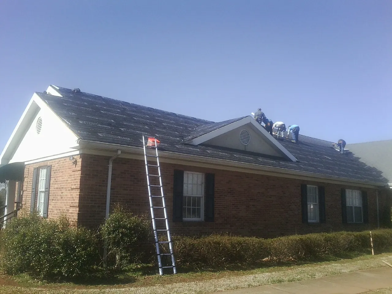 Crew tearing shingles off a brick ranch roof with a ladder set — Emergency Roof Repair work by our crew in Stanfield