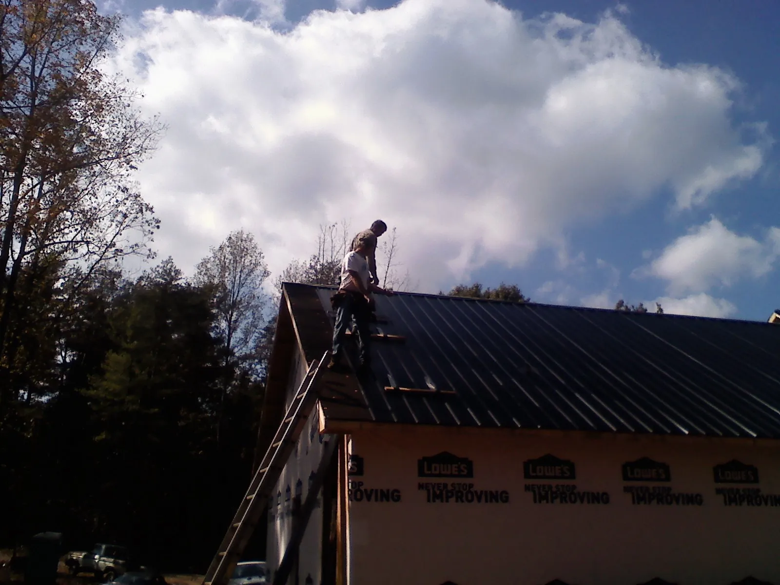 Roofer fastening dark metal panels high against a cloudy sky, from a Roof Inspection job in Stanfield